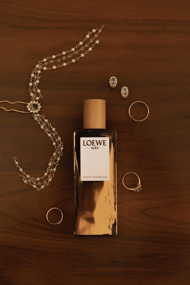 El perfume, los anillos y un collar sobre una mesa de madera oscura · Cupido debe morir