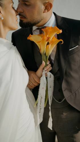 Beso de Rocío y Juan con el ramo de calas y la cinta bordada con la fecha de la boda