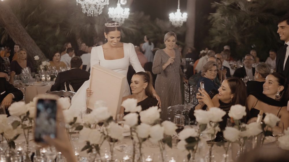 Patri stands up among the banquet tables, covered in white roses, as guests film her on their phones