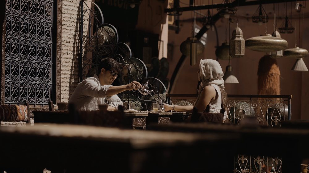 Patri and Juanma serve tea, seated beside a carved wooden lattice, in their pre-wedding in Morocco