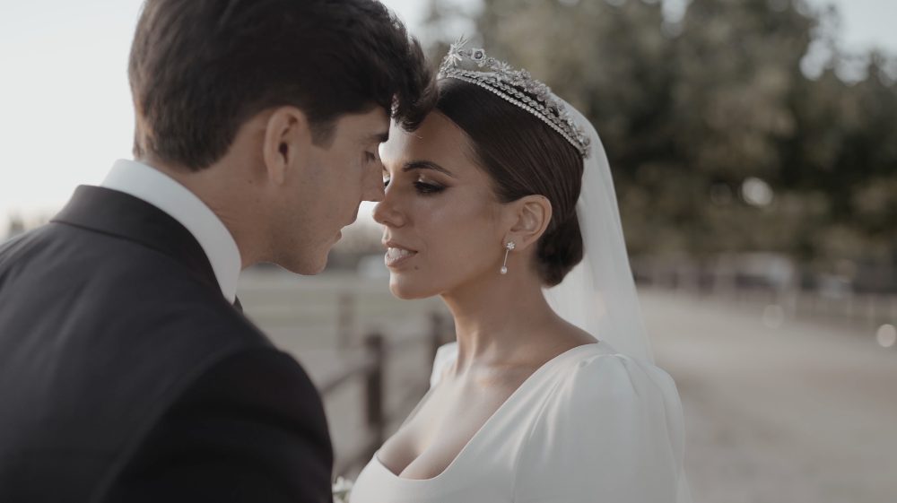 Patri and Juanma, forehead to forehead, with the tiara and veil, about to kiss