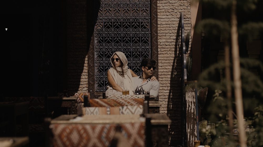 Patri, con pañuelo blanco y gafas de sol, junto a Juanma en una terraza con celosías y cojines de colores, en su preboda en Marruecos