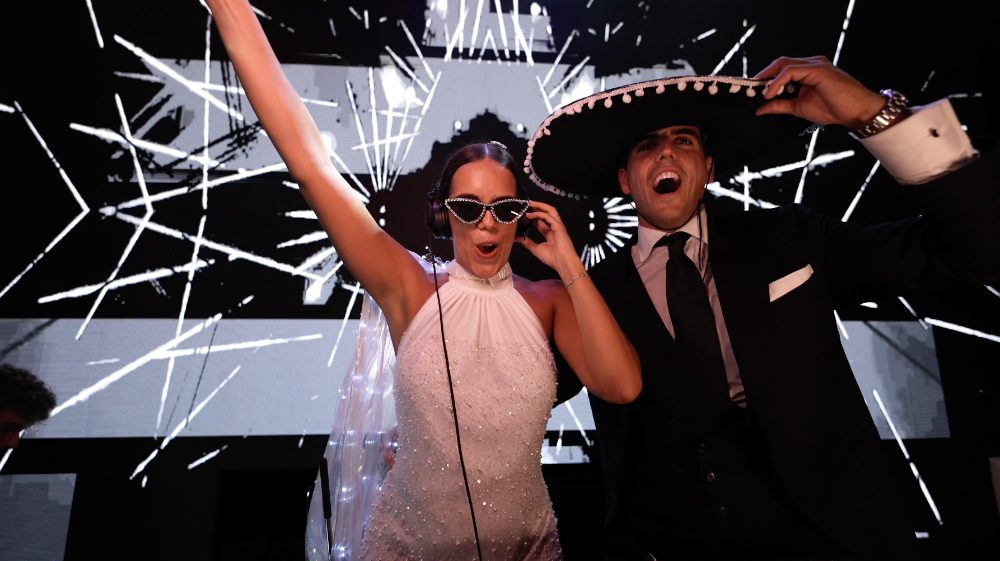 Patri y Juanma, con gafas y sombrero, bailan en la hora loca delante de unas pantallas de luces
