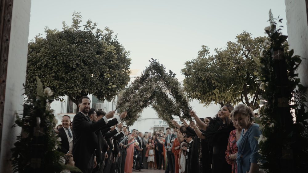 Un arco de hojas y flores a la salida de la ceremonia, con los invitados esperando debajo
