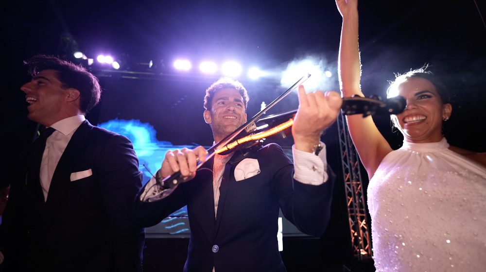 Un violinista toca en directo sobre el escenario, junto a Patri, que levanta la mano
