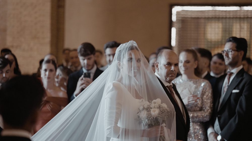 Patri enters the ceremony with her veil over her face, the guests looking at her