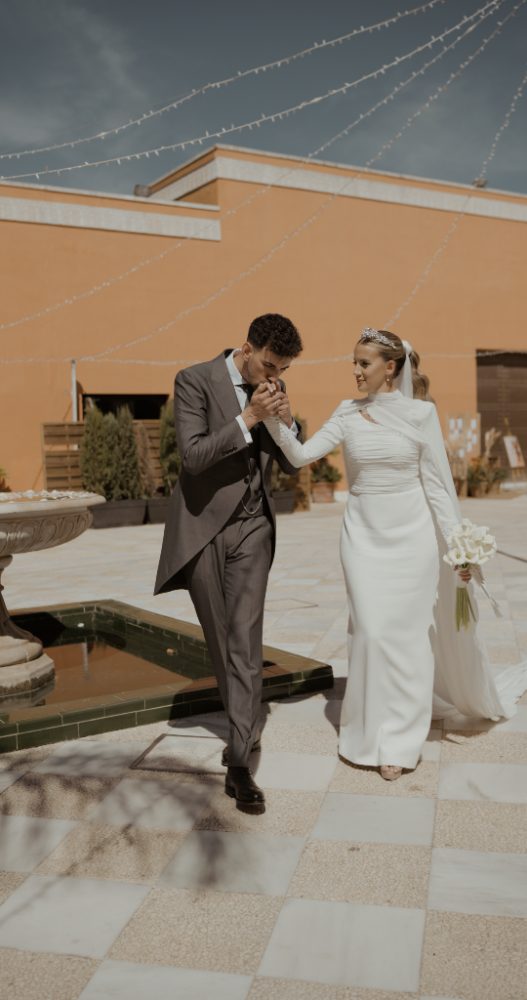 Edu besa la mano de Alicia en el patio de la Hacienda Al-Baraka, junto a una fuente y bajo guirnaldas de luces