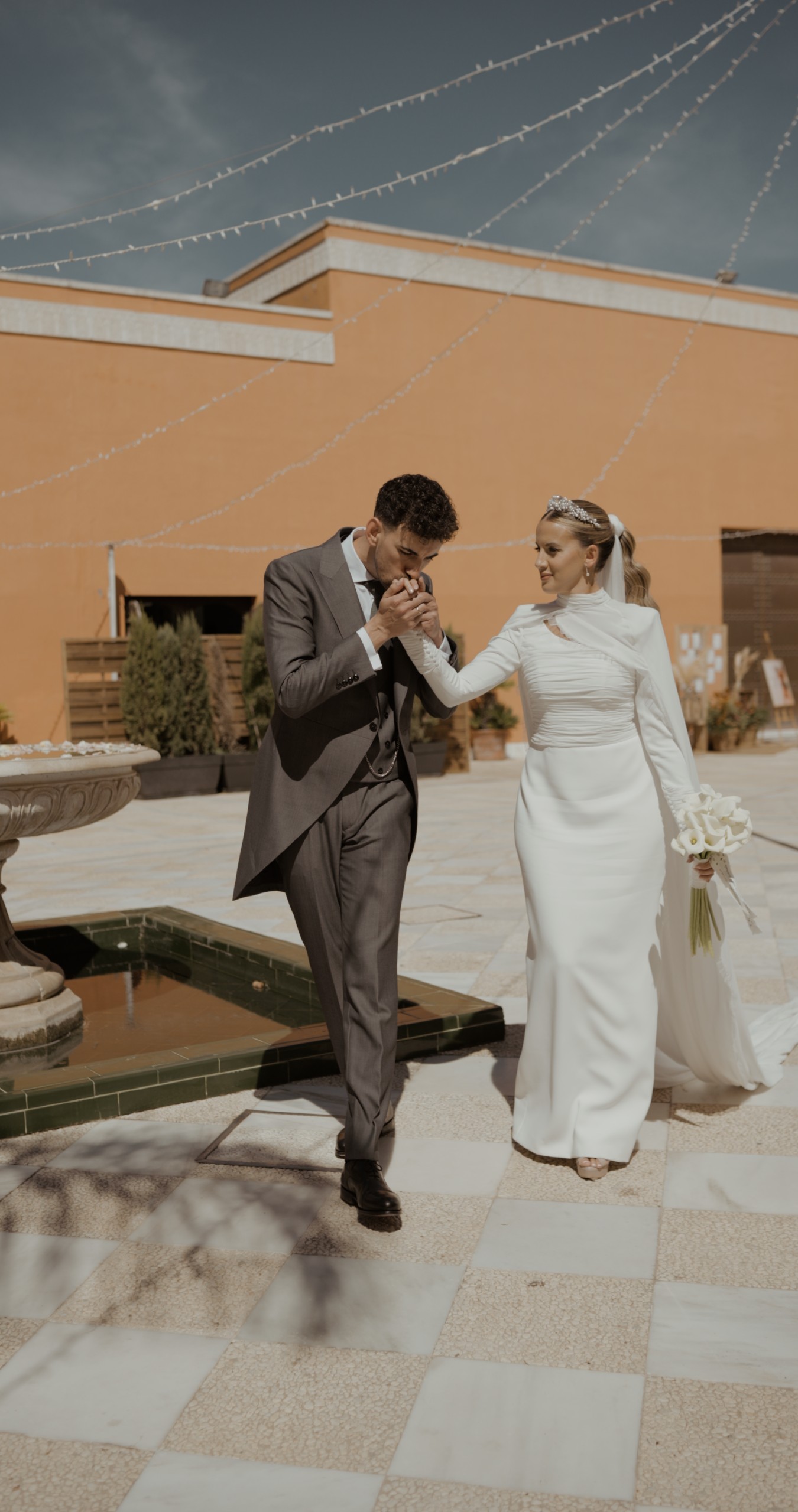 Edu besa la mano de Alicia en el patio de la Hacienda Al-Baraka, junto a una fuente y bajo guirnaldas de luces