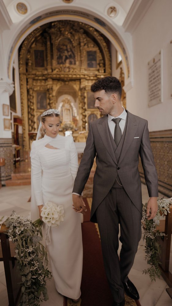 Alicia y Edu caminan de la mano por la nave de la Ermita de Nuestra Señora de Belén, en Pilas, ante el retablo dorado