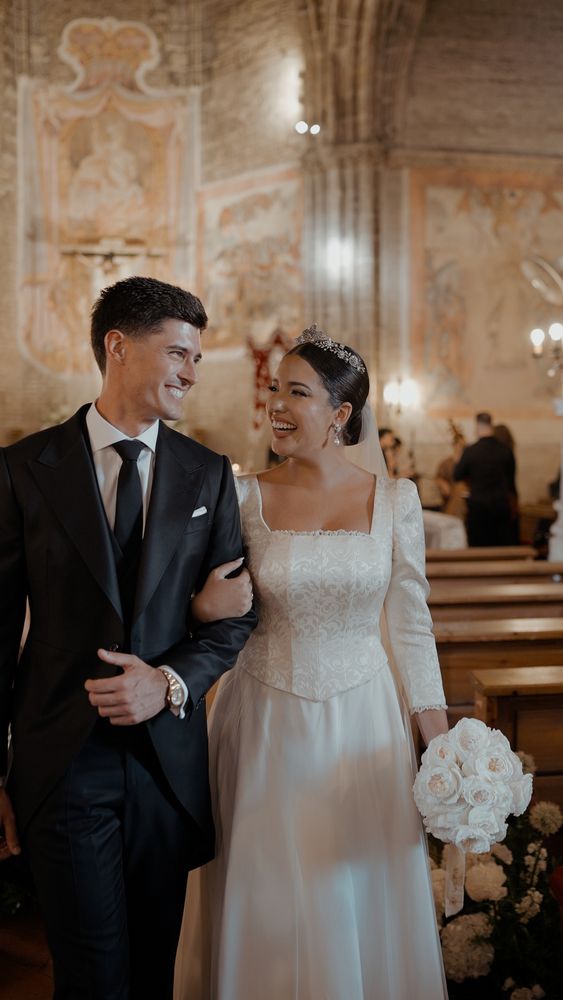 The couple leaving the convent church smiling, he in a morning coat, she with white roses · Gearmedia