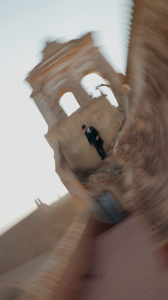 The same tower with a wide-angle twist and blur; the groom, tiny in the centre · Gearmedia