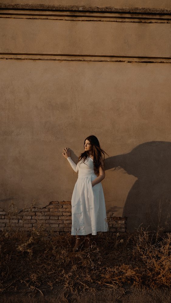 The bride in white against an adobe wall in golden light, her shadow cast on it · Gearmedia