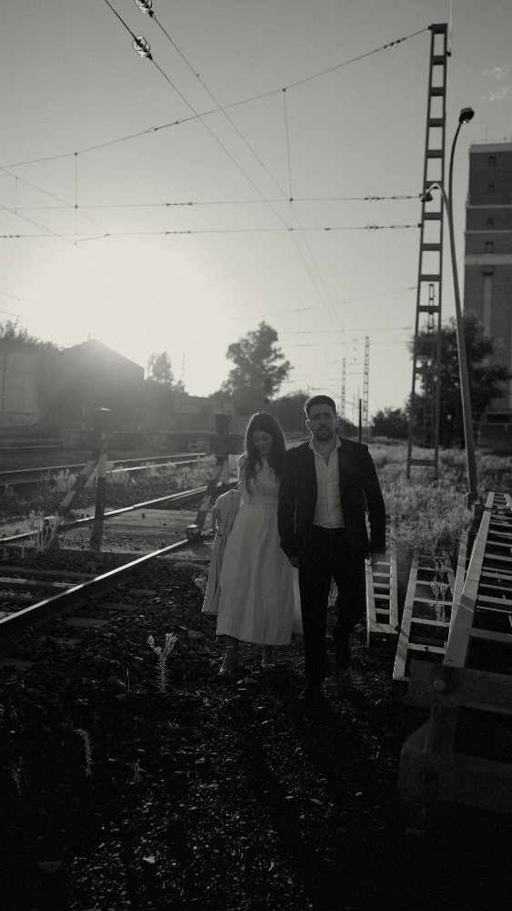 The couple walking along the railway tracks, backlit, with the overhead cables · Gearmedia