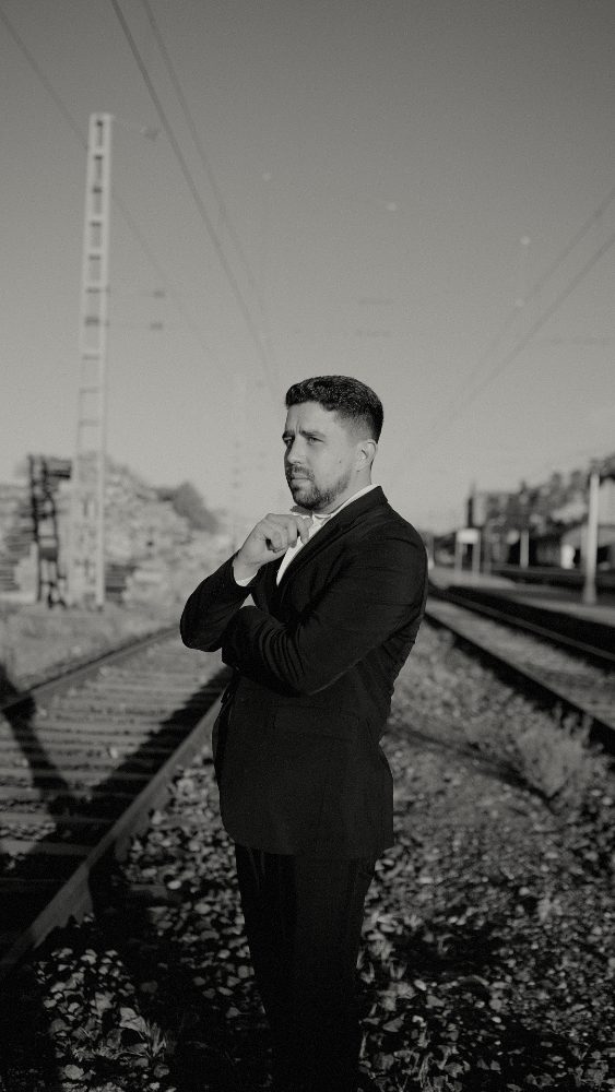 The groom in a suit adjusting his bow tie on the railway tracks, black and white · Gearmedia