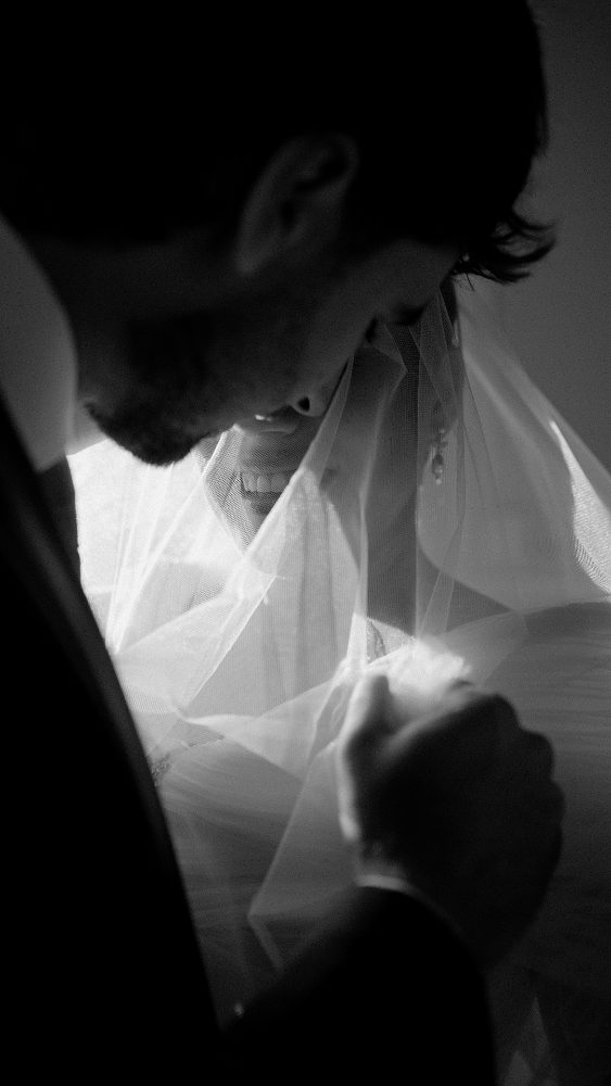 Black and white: the groom leaning over the veil, backlit · Gearmedia
