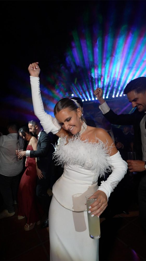 Rocío baila con un top de plumas blancas y un vaso en la mano, con los brazos en alto, entre luces de colores y sus invitados