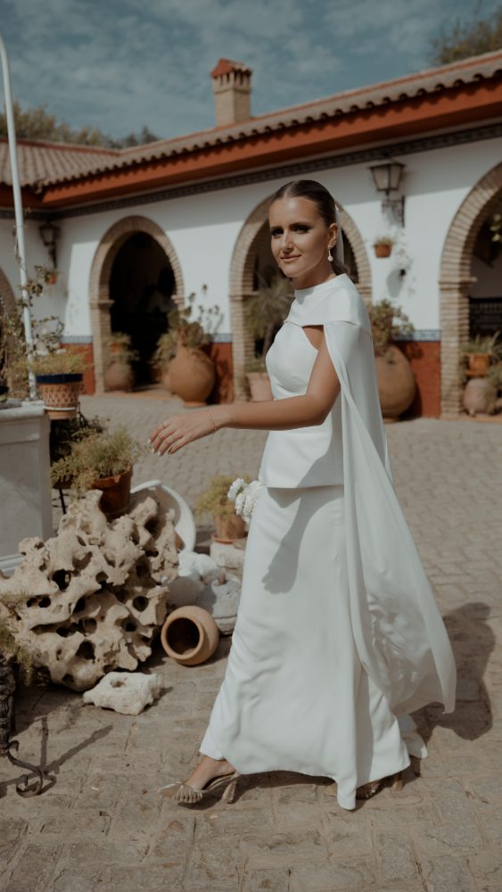 Rocío, de perfil y con la capa blanca extendida, camina junto a unas rocas y macetas de la finca