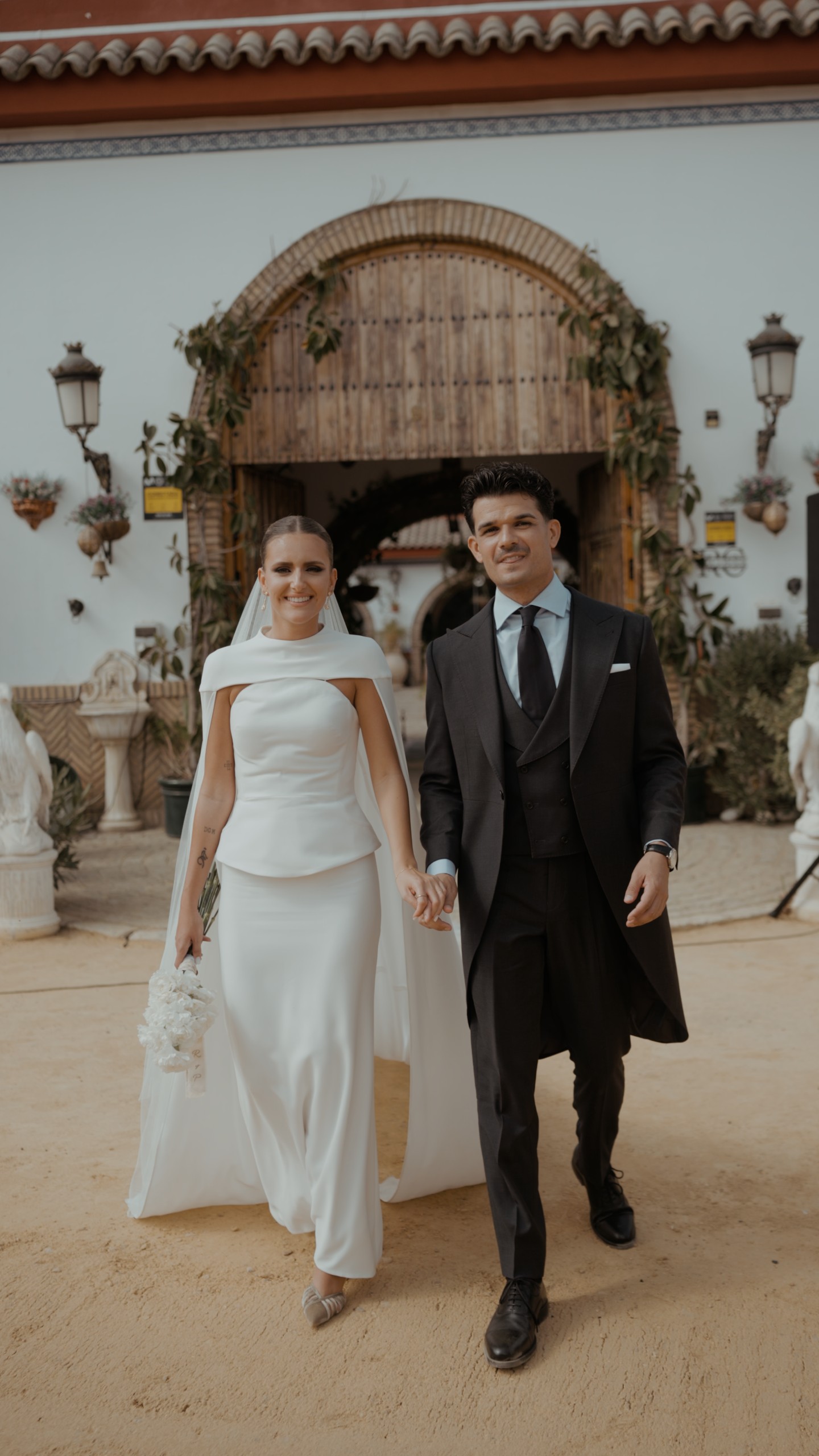 Pablo y Rocío, de la mano, salen por un portón de madera con enredadera hacia un camino de arena
