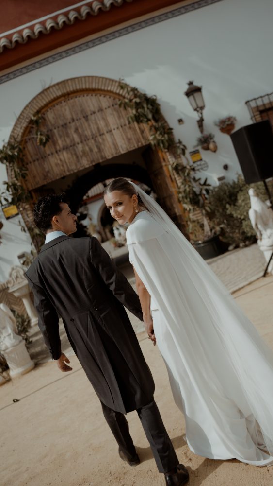 Pablo y Rocío, de la mano, se alejan por el camino de arena; ella mira atrás a cámara con el velo largo al aire