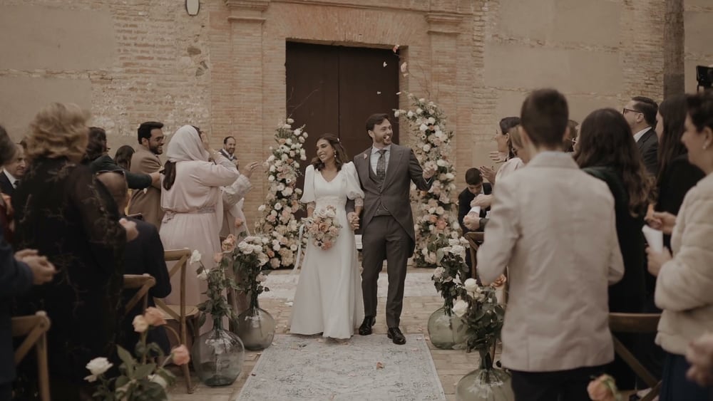Juan and May walk out of the ceremony down the aisle between their guests, between two arches of flowers at the church door of the Convento de la Luz