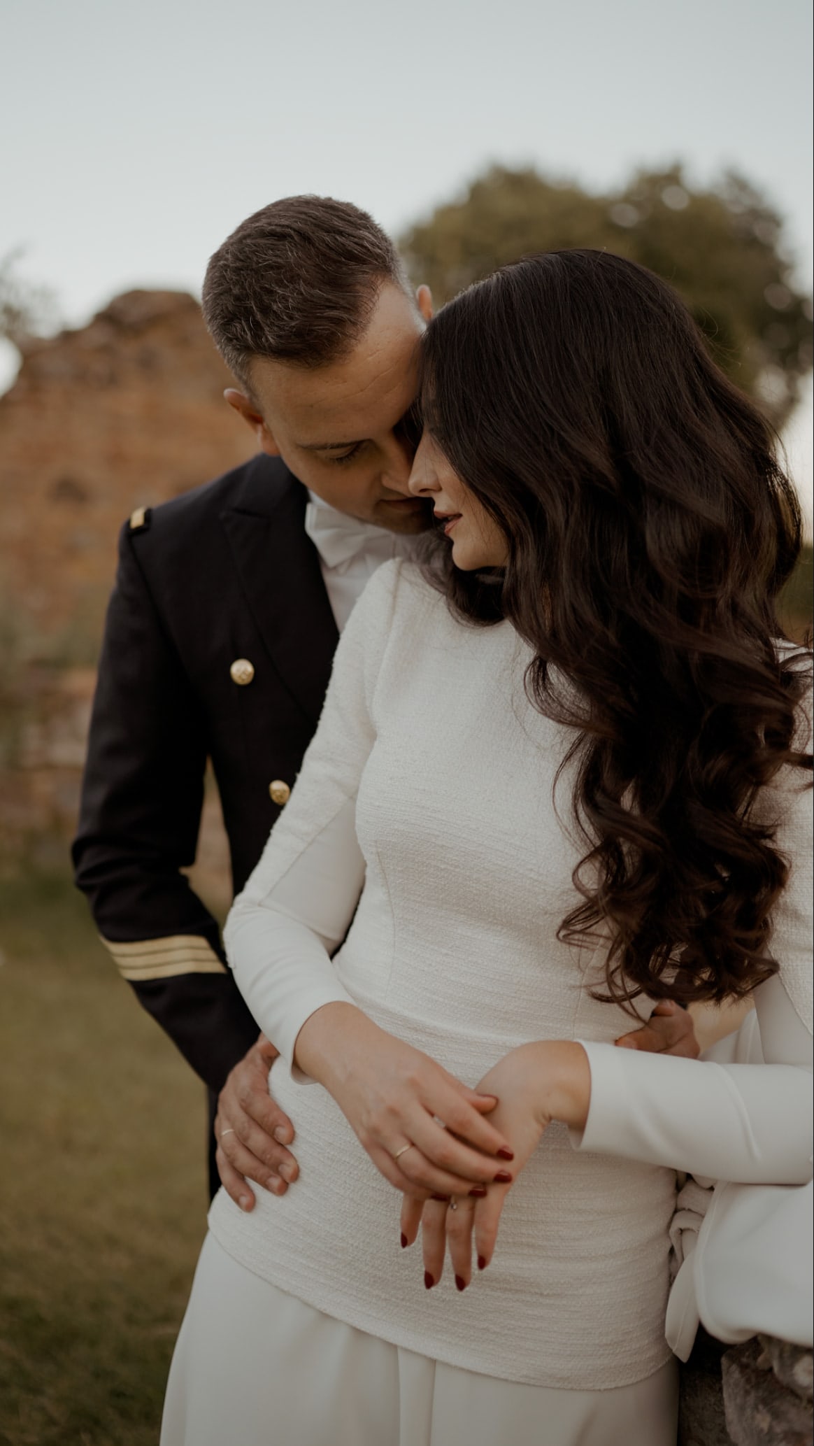 El novio, de uniforme, abraza a la novia por detrás, en La Cartuja de Cazalla, Sevilla