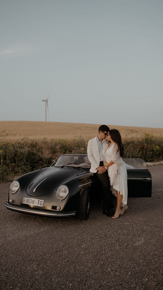Pareja junto a un Porsche clásico negro al lado de un campo de trigo · Gearmedia y Cupido debe morir