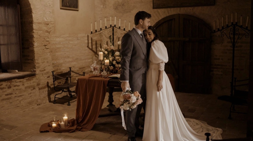 Novios abrazados en un salón de piedra con candelabros, en una boda en Sevilla · Gearmedia