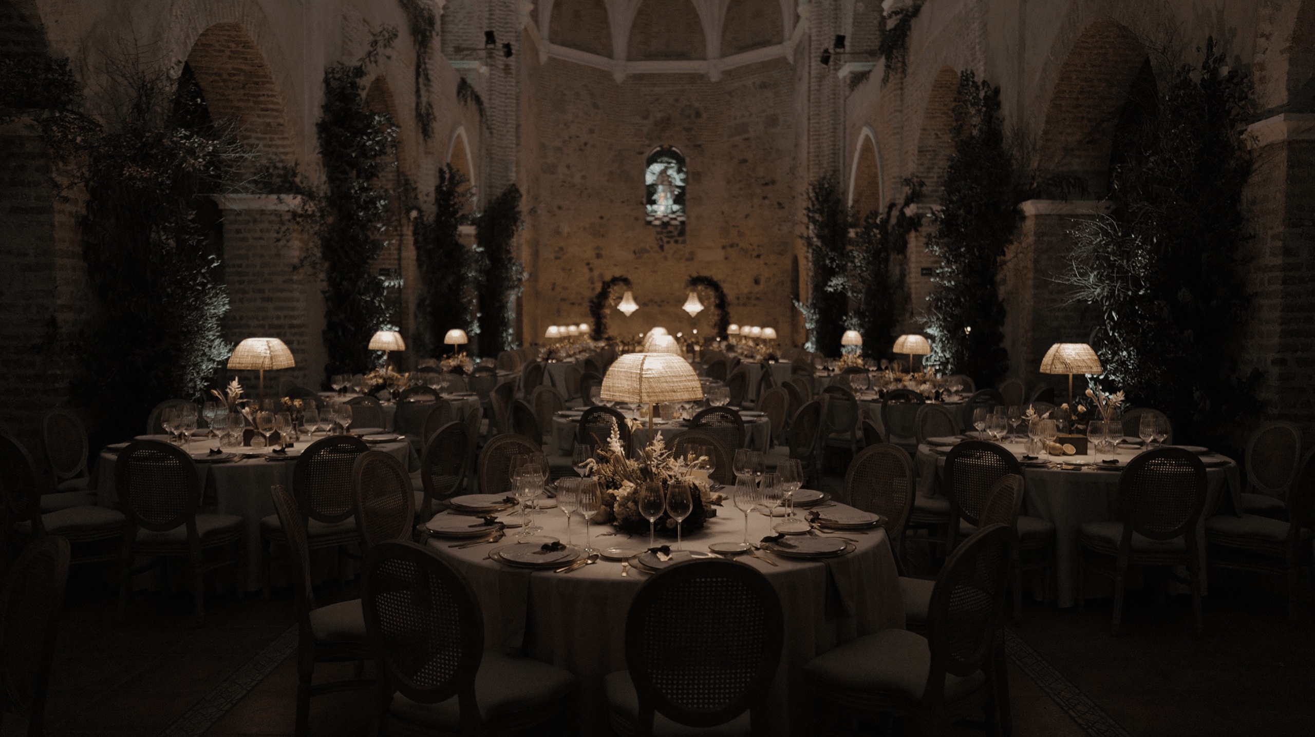 Salón del banquete con mesas redondas y lámparas bajo arcos de piedra, en una boda en Huelva · Gearmedia