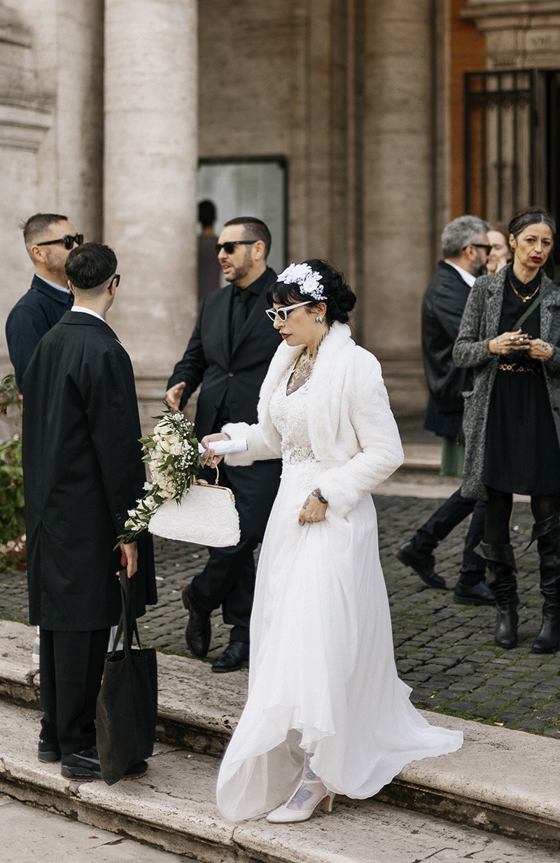Novia con abrigo de piel blanco subiendo unas escaleras entre invitados · Gonzalo Lagares