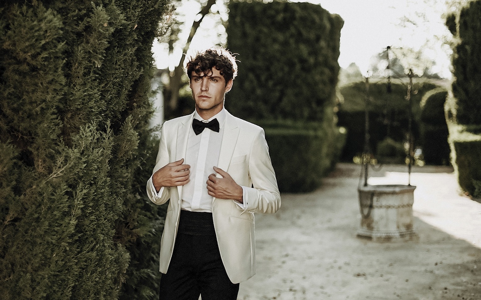 Novio con chaqueta blanca y pajarita en un jardín de setos · Gonzalo Lagares