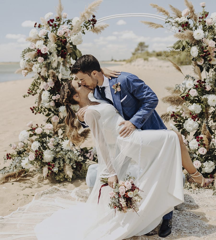 Novios besándose bajo un arco de flores en la playa · Gonzalo Lagares