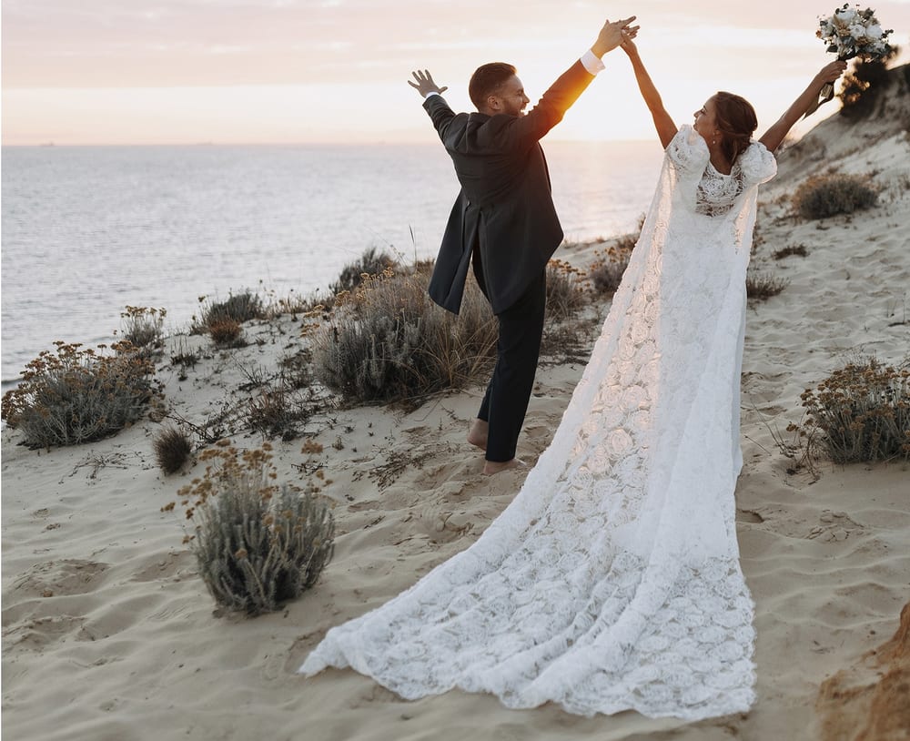 Novios con los brazos en alto sobre una duna junto al mar · Gonzalo Lagares